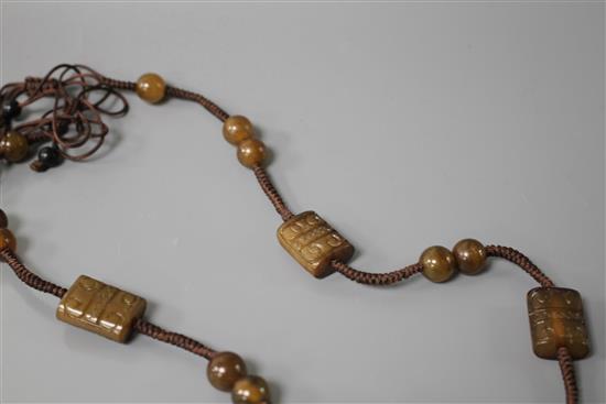 A Chinese hardstone necklace, with carved and inscribed plaque and brown fabric strung beads, plaque 6 x 4.5cm, rectangular beads 2cm a